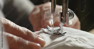 A hand of a young seamstress sewing a white cloth tailoring according to the tradition of tailors. The dressmaker uses perfectly needle and thread to sew traditional concept, sewing, style and fashion