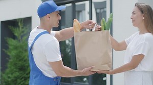 Beautiful woman meets a delivery man who gives her a shopping package with food beside her home. Food delivery. Concept of courier, home delivery, online shopping 5
