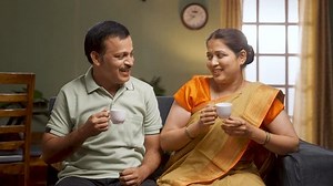 Happy smiling couple having tea or coffee while talking each other at home during morning - concept of family time, relaxation and refreshment