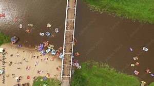 A bird's-eye- view shows people of all ages participating in Kaljakellunta, the beer floating festival in Finland, riding on inflatable boats and inner tubes down a river.