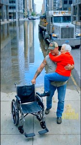 An elderly woman in a wheelchair got stuck in a large puddle on the road. Before anyone else reacted, a truck driver stopped, carefully carried her to safety, and brought her wheelchair as well. A quiet act that proved kindness still exists on our streets. #AI #kindness #heartwarming #gooddeeds #inspiration | Virum
