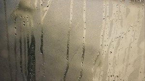 Hot weather conditions indoors - water droplets drip down glass window. Condensation on winter appearing due to changes in temperatures. Cold winter or very hot room indoor