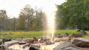 A video capturing the eruption of a hot spring geyser in a natural setting, with steam rising and surrounding greenery, showcasing the beauty of geothermal activity.
