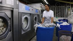 Female worker at a launderette pushing a heavy bin with dirty napkins...