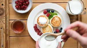 Syrniki or cottage cheese fritters with sour cream, berries and honey on a rustic wooden table, top view. 4k footage of serving cheese pancakes Stock-Video