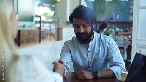 Close-up view from back of two male and female business partners shaking hands over coffee in coffee shop. Front view of business partners finish meeting in summer cafe. Shooting in slow motion.