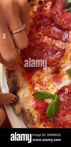 Caucasian teen biting pepperoni pizza slice, sunlit outdoor table, charred neapolitan crust, fresh basil, closeup hands with heart Stock Video Footage - Alamy