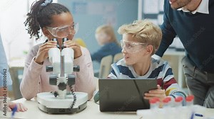 Elementary School Science Classroom: Cute Little Girl Looks Under Microscope, Boy Uses Digital Tablet Computer to Check Information on the Internet, while Enthusiastic Teacher Explains Lesson