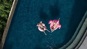 clip-1112133695-married-couple-sunbathing-swim-inflatable-pink-flamingo