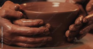 Hands of couple form a pot of clay on a potter's wheel. A female hand helps a man's hands shape a clay shape. Top view.