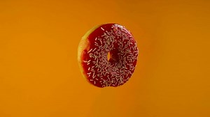 Delicious sweet donut rotating on a plate. Bright and colorful sprinkled donut on an orange background. Close-up. 4K