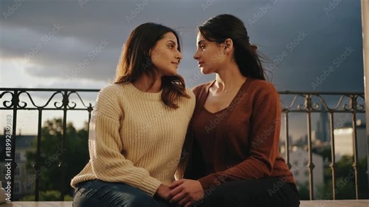 Two women sharing a tender moment on a balcony at sunset