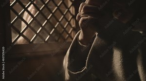 Mid adult religious woman praying near confessional booth window. Female parishioner sitting with clasped hands during confession in church close up