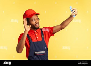 Smiling friendly workman wearing blue overalls taking selfie or having video call with client, waving hand, saying hello, being ready to execute order Stock Photo - Alamy