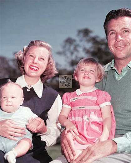 "June Allyson and her husband, Dick Powell, are photographed at their Los Angeles home circa 1951, surrounded by their children, Pamela and Richard, in a moment that captures the golden domestic image of classic Hollywood. Powell, a versatile performer turned director, had transitioned into behind-the-scenes roles by then, while Allyson remained one of MGM’s most bankable stars. Their Spanish-style home in Toluca Lake served as the backdrop for many such family moments, blending star power with 