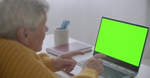 Mature woman nodding her head yes while looking at a green screen computer. Elderly mature woman with gray hair and a video call on her Laptop. Laptop with a green screen