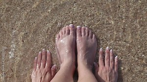 Top view video footage of barefeet female legs and hands washing by warm sea water at beach. Fingernails with beautiful pink and white french pedicure. Happy woman enjoying summer vacations concept.