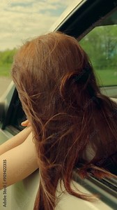 Beautiful girl travels look from car window, wind blowing her hair. Young woman passenger looks out window, enjoys fresh breeze from car window. Road trip on way to vacation. Happy look into future