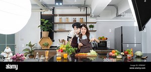 Asian couple spend time together in the kitchen. Young woman in apron cooking salad dish while his boyfriend recording vlog video for social blogger. Photography studio lights set up in the kitchen Stock Photo - Alamy