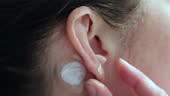 A woman is applying pressure on her acupuncture magnets on her ears...
