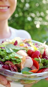 Sporty Woman Eating Vegetarian Salad. Fresh colored salad with lettuce leaves and tomato into bowl, served with healthy food ingredient. Family dinner with organic salad, top view. Summer food outdoor