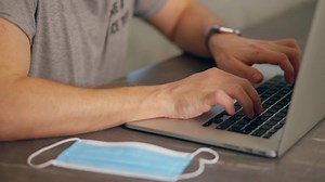 Upset and angry man hits laptop with fist and face mask then leaves