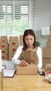 A young Asian entrepreneur happily works in her office, managing online retail orders and shipping packages, using technology to make her startup successful and grow.