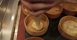 A large plastic syringe with cream inside fills the tartlets. Close-up of the cream flowing from the pastry syringe and filling the tartlet.