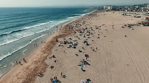A Vibrant Beach Scene featuring Sunbathers, Waves, and Sunlight on a Beautiful Sunny Day