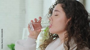 Woman waking up in morning and drinking a glass of water, girl dressed in white robe.