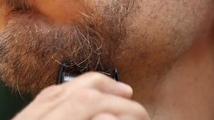 man shaves his beard on chin by trimmer, closeup