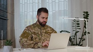 Male army soldier in military uniform using portable computer for emailing and working while sitting at home. Focused caucasian man typing at laptop keyboard and sending messages to commander office. Видео Stock