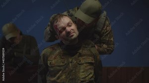 Portrait of injured prisoner of war in camouflage during interrogation indoors. Brutal male soldier intimidating enemy, putting gun to captive head, getting information from combatant