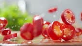 Freshly chopped red ripe chili peppers are thrown onto the wet wooden...