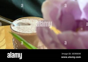 purple tulip hot cocoa with beige creamy foam, teaspoon lifting foam texture, purple tulip nearby, green background and wooden table, cozy mood, dessert drink concept Stock Video Footage - Alamy