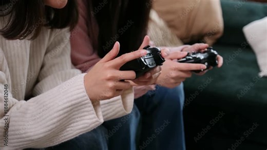 Two young women playing a video game together at home while sitting on the couch