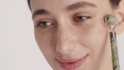 Positive woman with natural beauty massaging her face with jade stone...