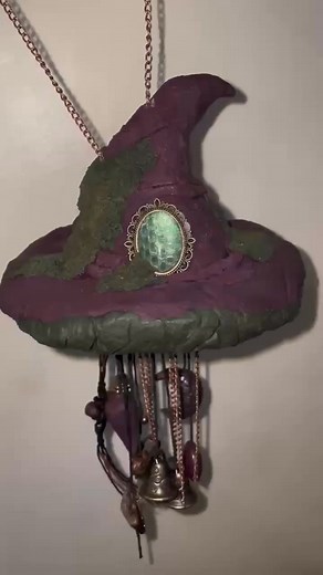 Witches Hat Wind Chime - Witches Bell Chime Hat. Size approx. 18 inches long x 6 inches wide. Handcrafted in Polymer Clay, with a real snake-skin charm, captured in resin, which decorates the front. Lots of moss, three brass bells, a hand-crafted dark raven skull, a crescent moon, crystals, metal hearts, chains, charms and more. Available from Dark Crescent Moon or our sister page Witches Warren | Dark Crescent Moon