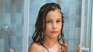 Little girl closes shower unit door and then opens it with smile on her face