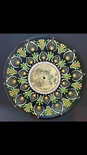 Reminisce about the unique fusion of rock, jazz, and Latin music with Santana Moonflower. Featuring a label with a moon graphic and earthy toned mandala dot painting on this vinyl record. This piece of wall art is a must-have for any music art enthusiast. Elevate your space with the greens, gold, and white tones and embrace the vibrant energy of Santana's iconic style. More here - https://thedottingchick.com/products/santana-moonflower #thedottingchick #musiclover #mandala #artmusic #MusicMemori