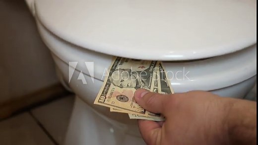 Paper dollars are clamped by the toilet lid. The concept of money being flushed down the toilet.