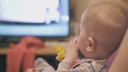 cute little child eats boiled corn on cob in mother arms watching tv...
