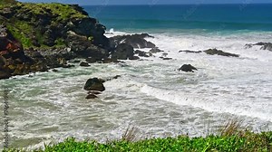 Australian coast, view from a cliff to the blue ocean with a rocky shore on a sunny day. Sea landscape, waves crashing on volcanic rocks at the shore.