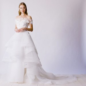 This romantic #JennyPackham wedding dress features a flattering off-the-shoulder neckline adorned with 3D flowers detailing with a statement tiered ruffle skirt. 🌷🌷 https://bit.ly/38tP5Zw | Designer Bridal Room, Hong Kong