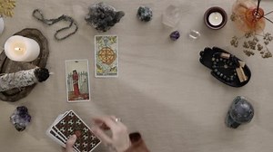New York, USA - 1 May 2021: Fortune teller woman with tattoos at her fingers reading a future by tarot cards while putting it picture up on the table. Esoteric concept, fortune telling predictions.