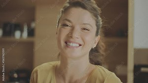 Close-up portrait shot of a young woman looking at camra and smiling while standing in the kitchen. Shot in slow-motion