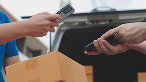Download Fast and reliable service. Cheerful young delivery man giving a cardboard box to young woman while standing at the entrance of her apartment for free