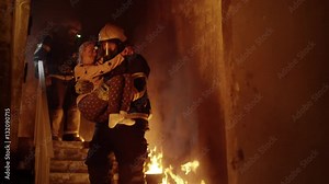 Burning Building. Group Of Firemen Descend on Burning Stairs. One Fireman Holds Saved Girl in His Arms. Shot on RED EPIC (uhd).