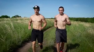 Two shirtless muscular men exer ising in nature in summertime.