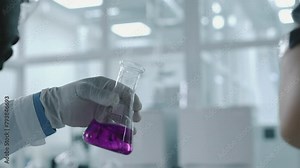 Close-up rear shot of multiethnic male and female chemists standing in laboratory, examining flask with purple permanganate solution, discussing colour, checking for residue